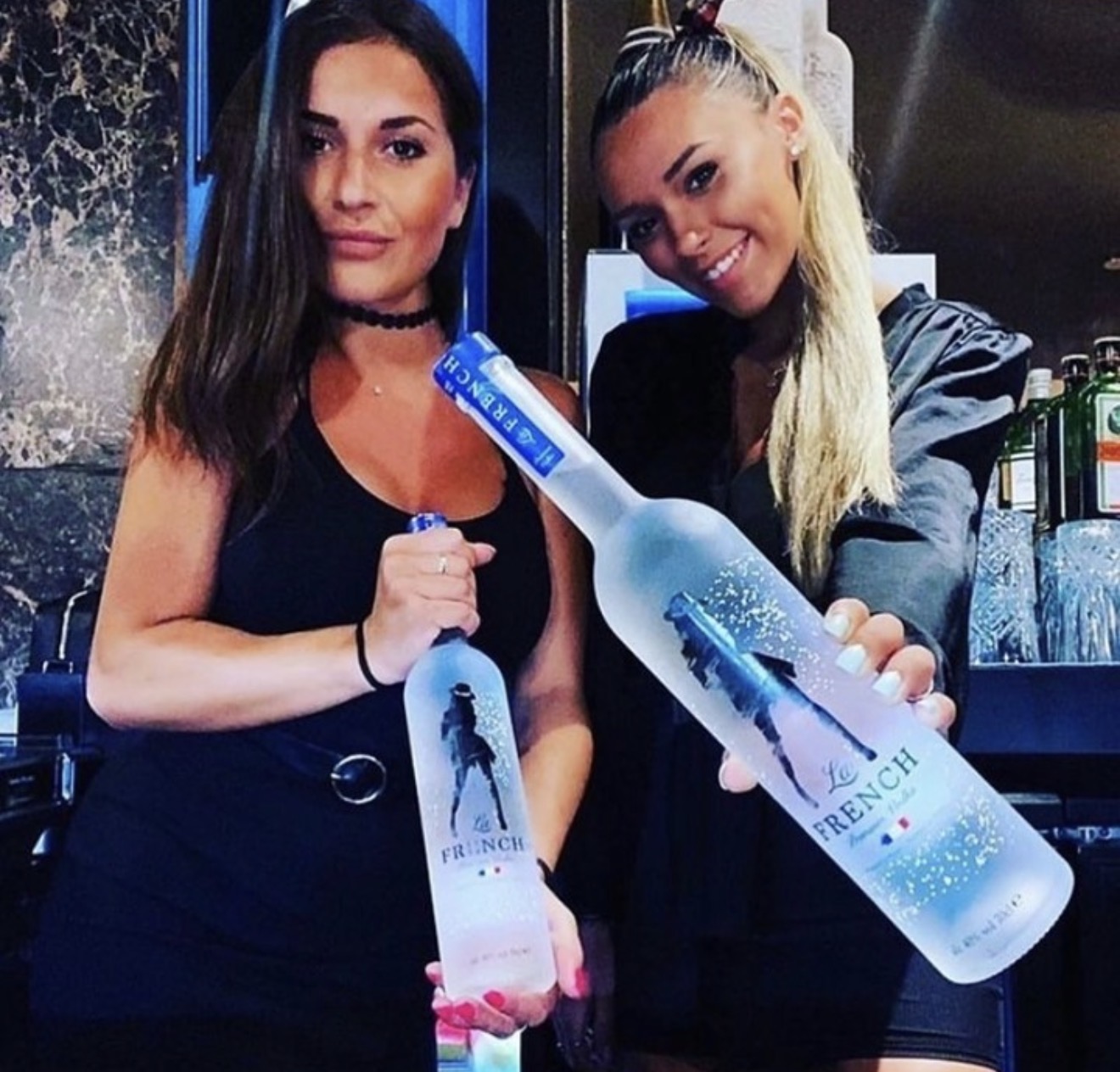 Friends holding La French Vodka bottles at a bar